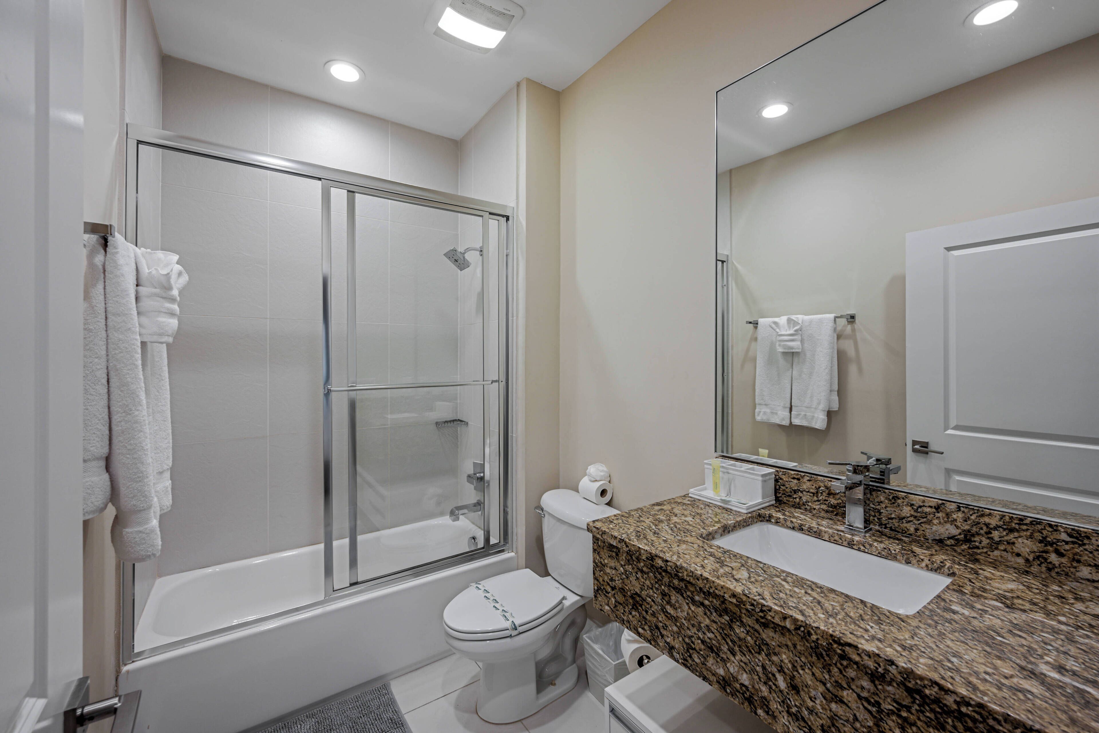 Un baño moderno con ducha de vidrio, inodoro blanco y lavamanos sobre encimera de granito.