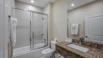 Un baño moderno con ducha de vidrio, inodoro blanco y lavamanos sobre encimera de granito.