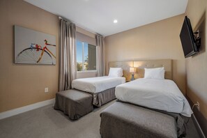 Una camera d'albergo con due letti, una finestra con tende, una TV a parete e un quadro appeso.