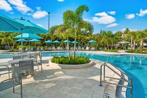 Uma área de piscina com espreguiçadeiras, guarda-sóis e um pequeno jardim.