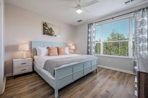 Ein Schlafzimmer mit Bett, Nachttischen, Deckenventilator, Fenster mit Jalousien und Wandkunst.