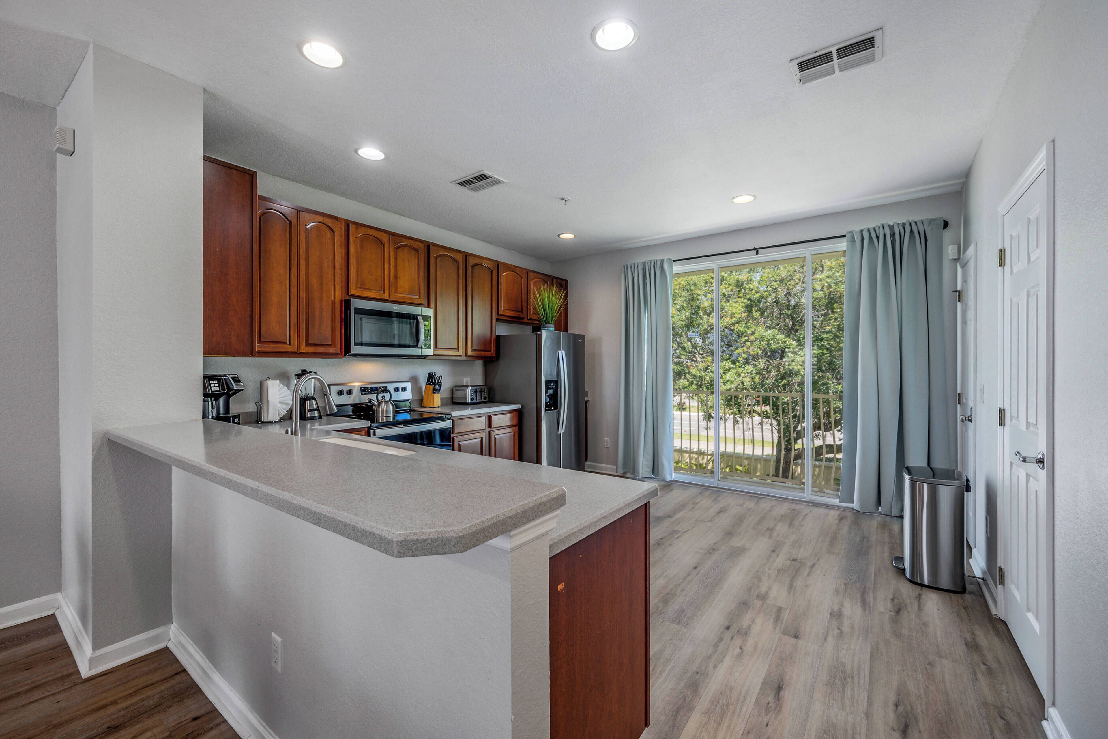 A modern kitchen with wooden cabinets, a granite countertop, and a large window with curtains.