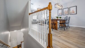 Un interior moderno con una escalera de madera, barandilla blanca y una zona de comedor con sillas y una mesa.