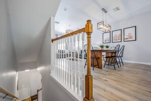 Un intérieur moderne avec un escalier en bois, une rampe blanche et un coin repas comprenant des chaises et une table.