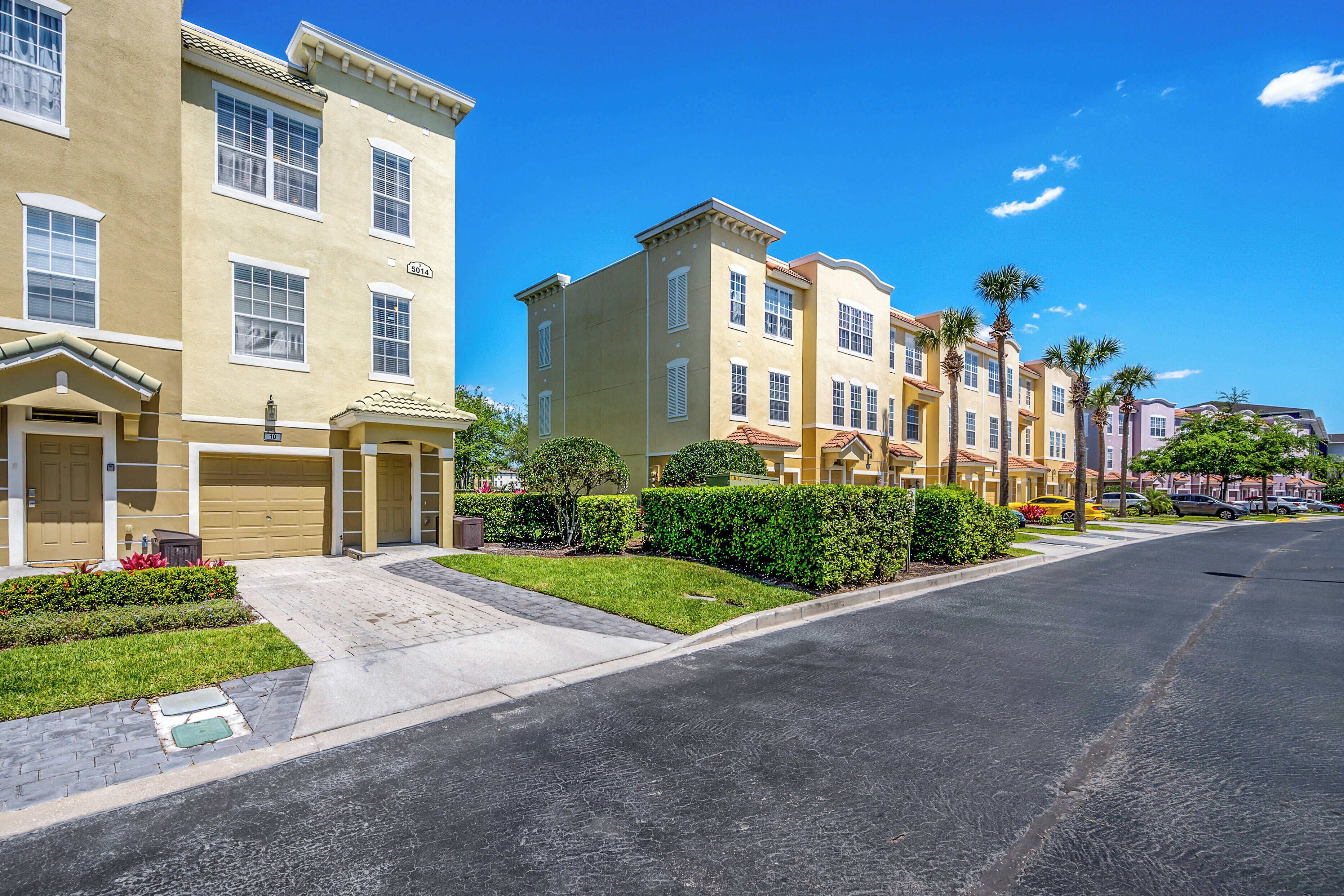A row of townhouses with a garage, a well-maintained lawn, and a clear blue sky.