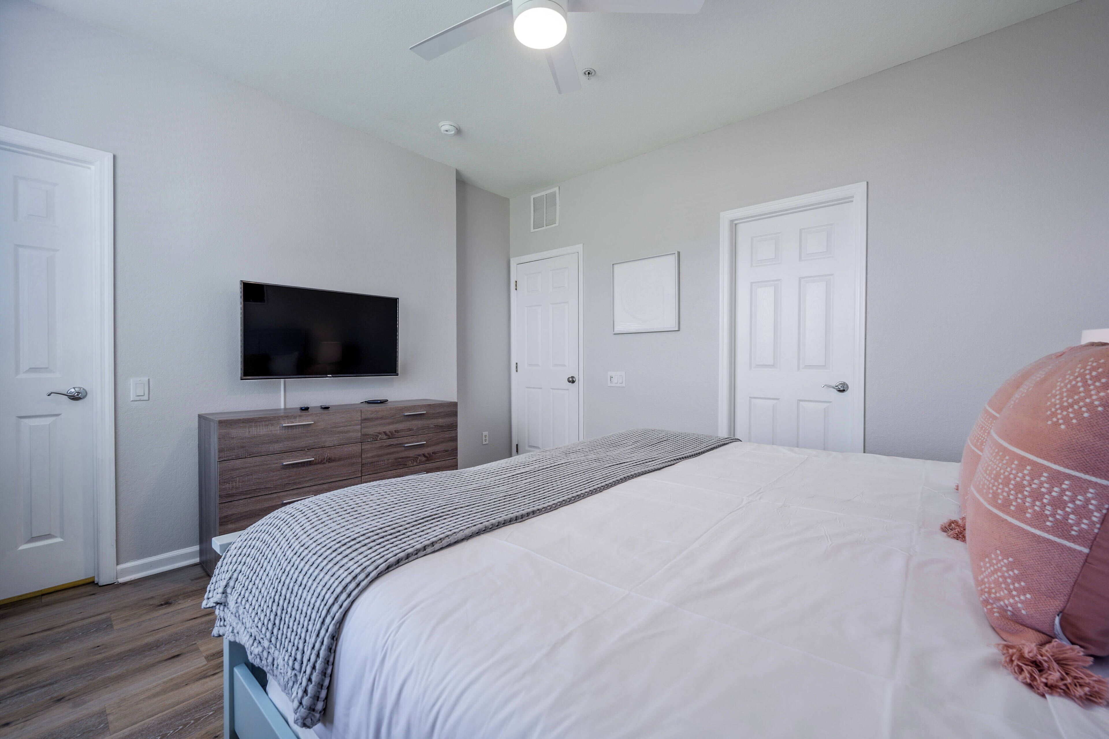 A bedroom with a bed, a dresser, a television, and two doors.
