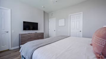 A bedroom with a bed, a dresser, a television, and two doors.