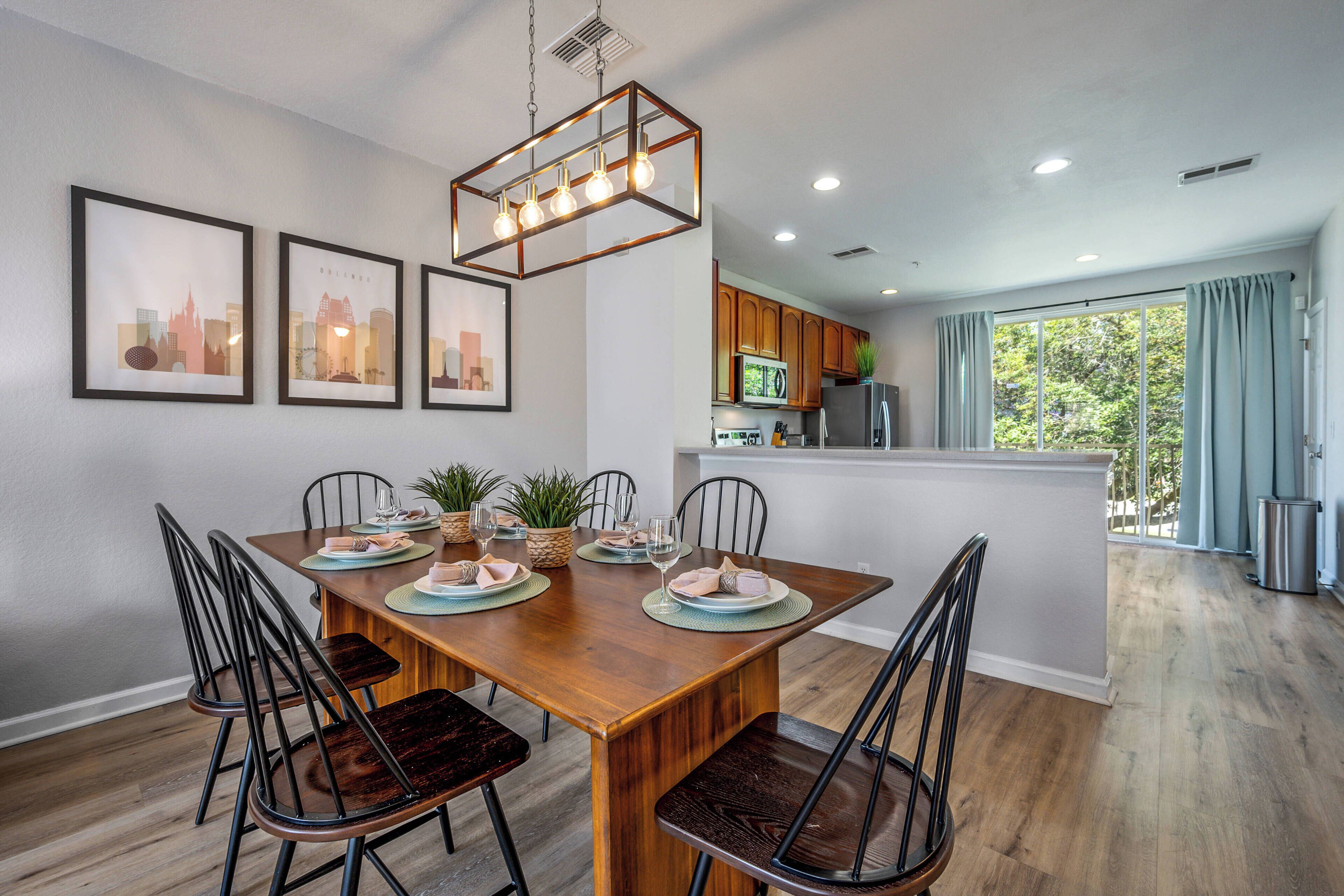 A dining area with a wooden table, six chairs, and a hanging light fixture.