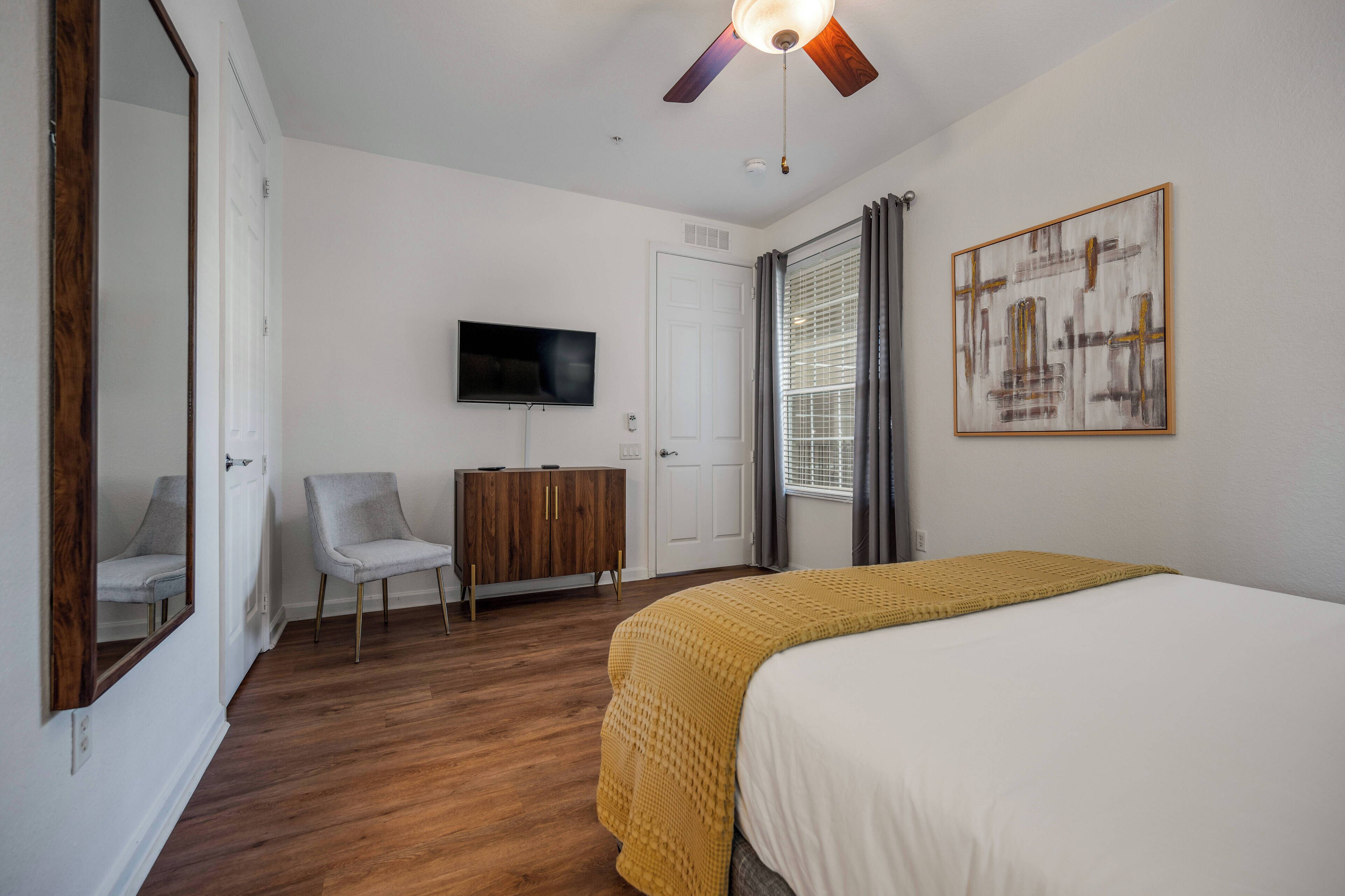Een slaapkamer met een bed, een televisie, een kledingkast, een stoel en een plafondventilator.