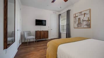 Een slaapkamer met een bed, een televisie, een kledingkast, een stoel en een plafondventilator.