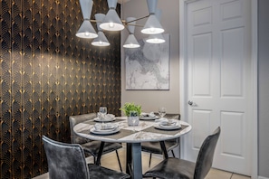 A dining area with a round table, black chairs, and a chandelier. There is a plant on the table and a door in the background. - Vc6-105 - 3BR Condo Resort Access Near Disney (Orlando)