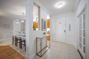 A modern kitchen with white cabinetry, a marble countertop, and a built-in oven. There is a dining area with a bar stool and a small table. - Vc6-105 - 3BR Condo Resort Access Near Disney (Orlando)