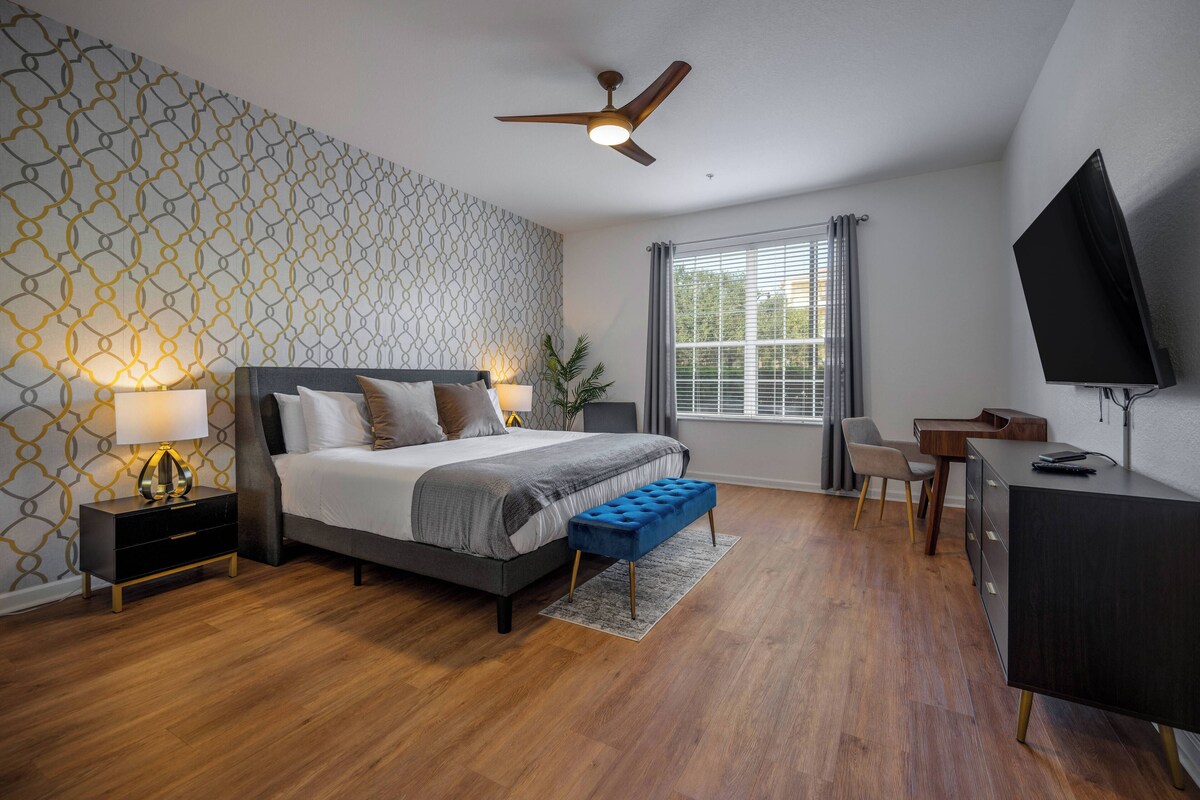 A modern bedroom with a bed, bedside tables, a desk, a television, and a window with curtains.