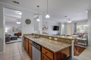 Eine moderne Küche mit Granit-Arbeitsplatten, einem Geschirrspüler und einem Essbereich mit grauem Sofa und Wand-Fernseher.
