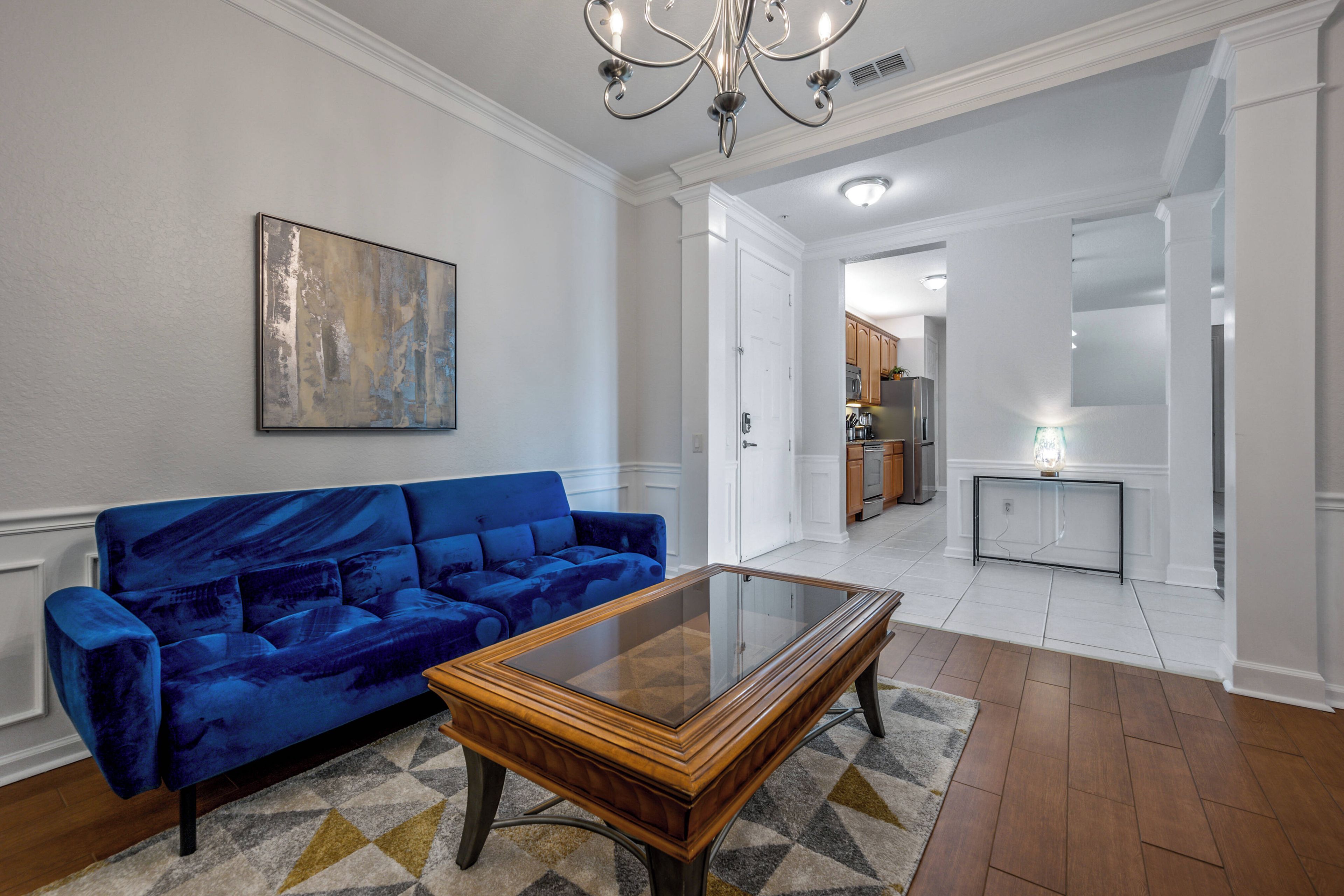 A living room with a blue sofa, a glass-top coffee table, and a painting on the wall.