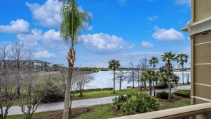 A view from a balcony overlooking a lake with palm trees and a building in the background. - Vc12-206 - 3BR Condo Lake View Near Disney (Orlando)