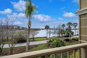 A view from a balcony overlooking a lake with palm trees and a building in the background. - Vc12-206 - 3BR Condo Lake View Near Disney (Orlando)
