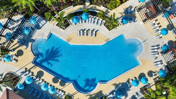 An aerial view of a resort with a large swimming pool, sun loungers, and palm trees. - Vc12-206 - 3BR Condo Lake View Near Disney (Orlando)