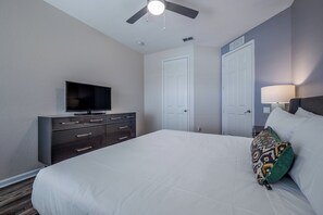 Ein Hotelzimmer mit Bett, Fernseher auf einem Schminktisch, Deckenventilator und einer Tür.