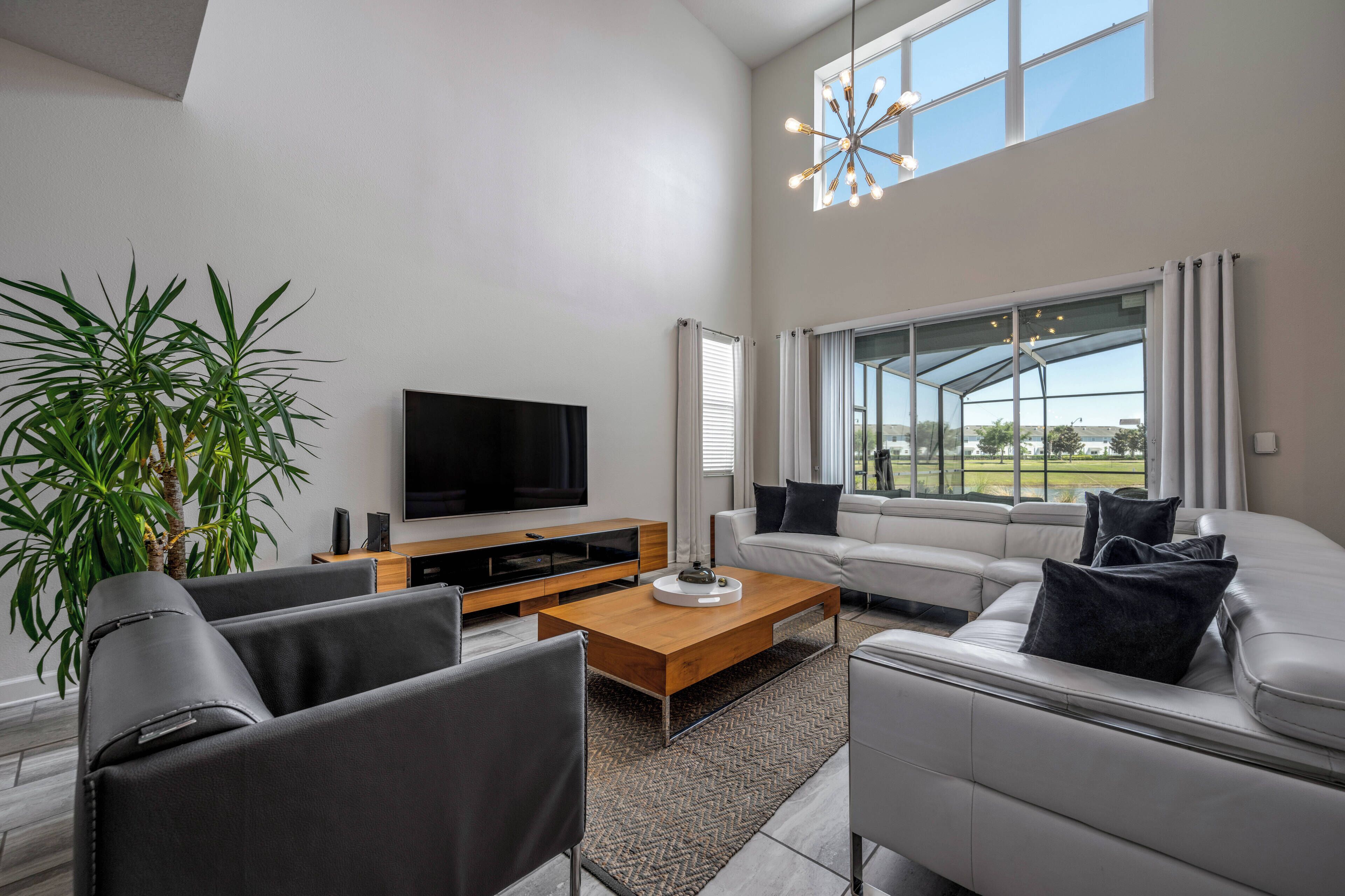 A modern living room with a sofa, chairs, a coffee table, a TV, and a large window with curtains.