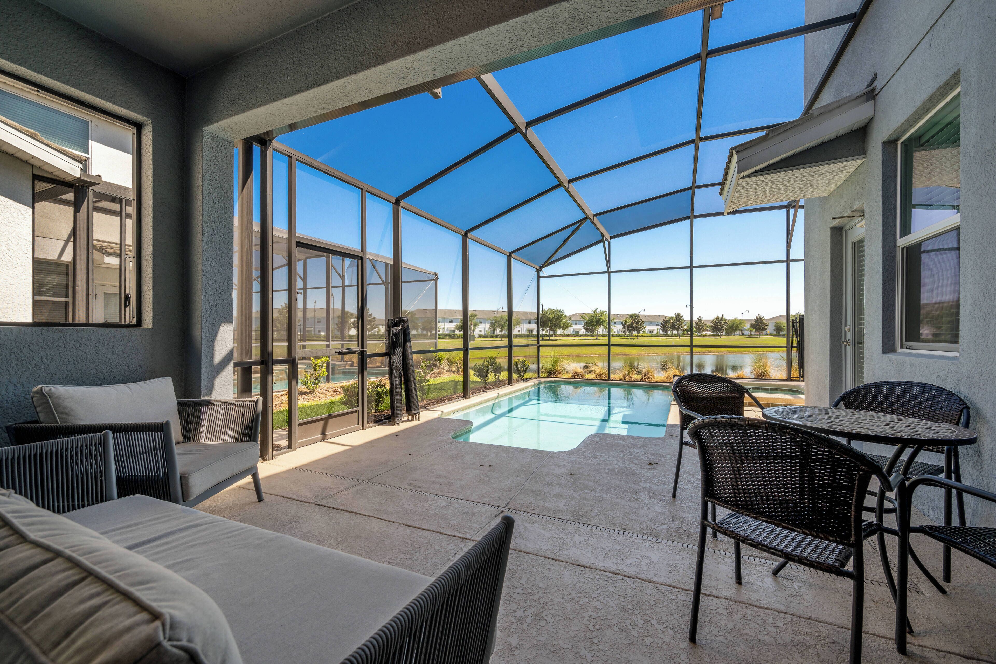A covered outdoor area with a pool, seating, and a view of a golf course.