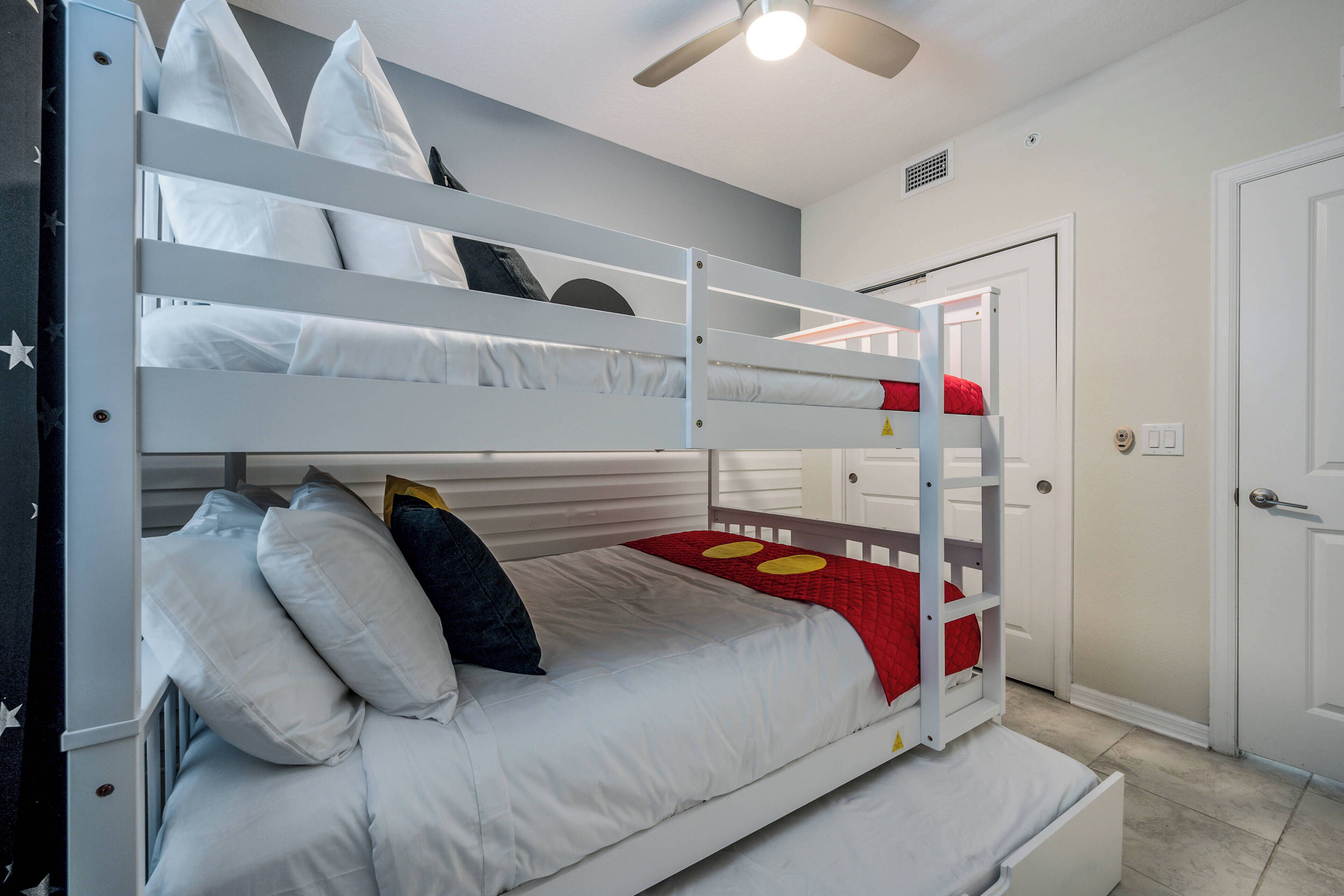 Habitación con literas, ropa de cama blanca, ventilador de techo y una puerta al fondo.
