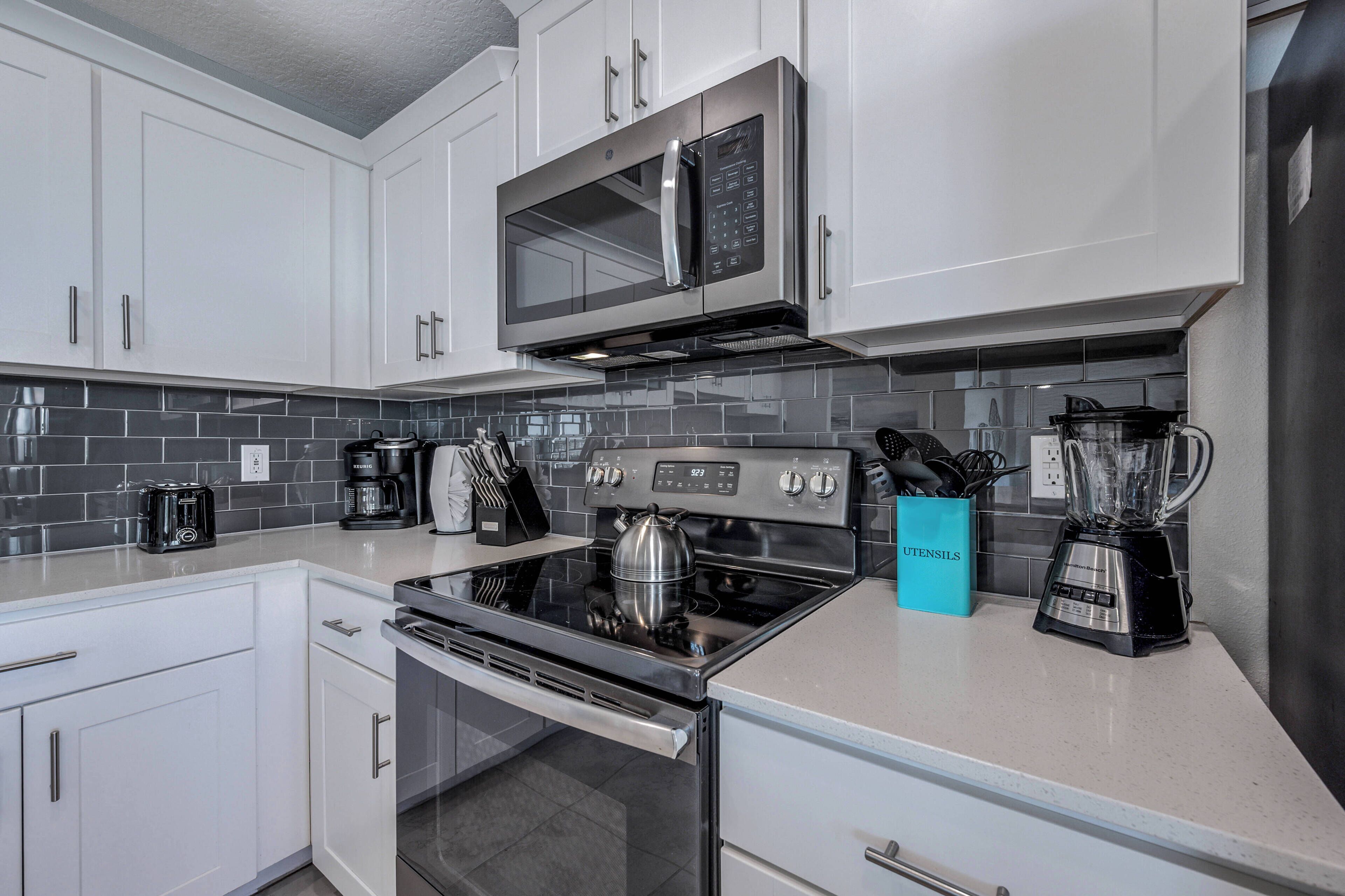 A modern kitchen with white cabinets, a stainless steel microwave, a gas stove, and a blender.