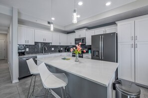 Une cuisine moderne avec des meubles blancs, un îlot central doté de tabourets, un réfrigérateur en acier inoxydable et un four à micro-ondes.