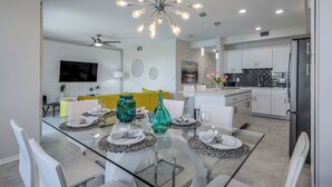 Una cocina moderna con armarios blancos, un refrigerador negro y un comedor con mesa de vidrio y sillas blancas.