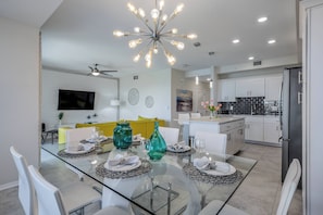 A modern kitchen with white cabinets, a black refrigerator, and a dining area with a glass table and white chairs. - Sl4721-307 - 2BR Apartment Near Disney Attractions (Kissimmee)