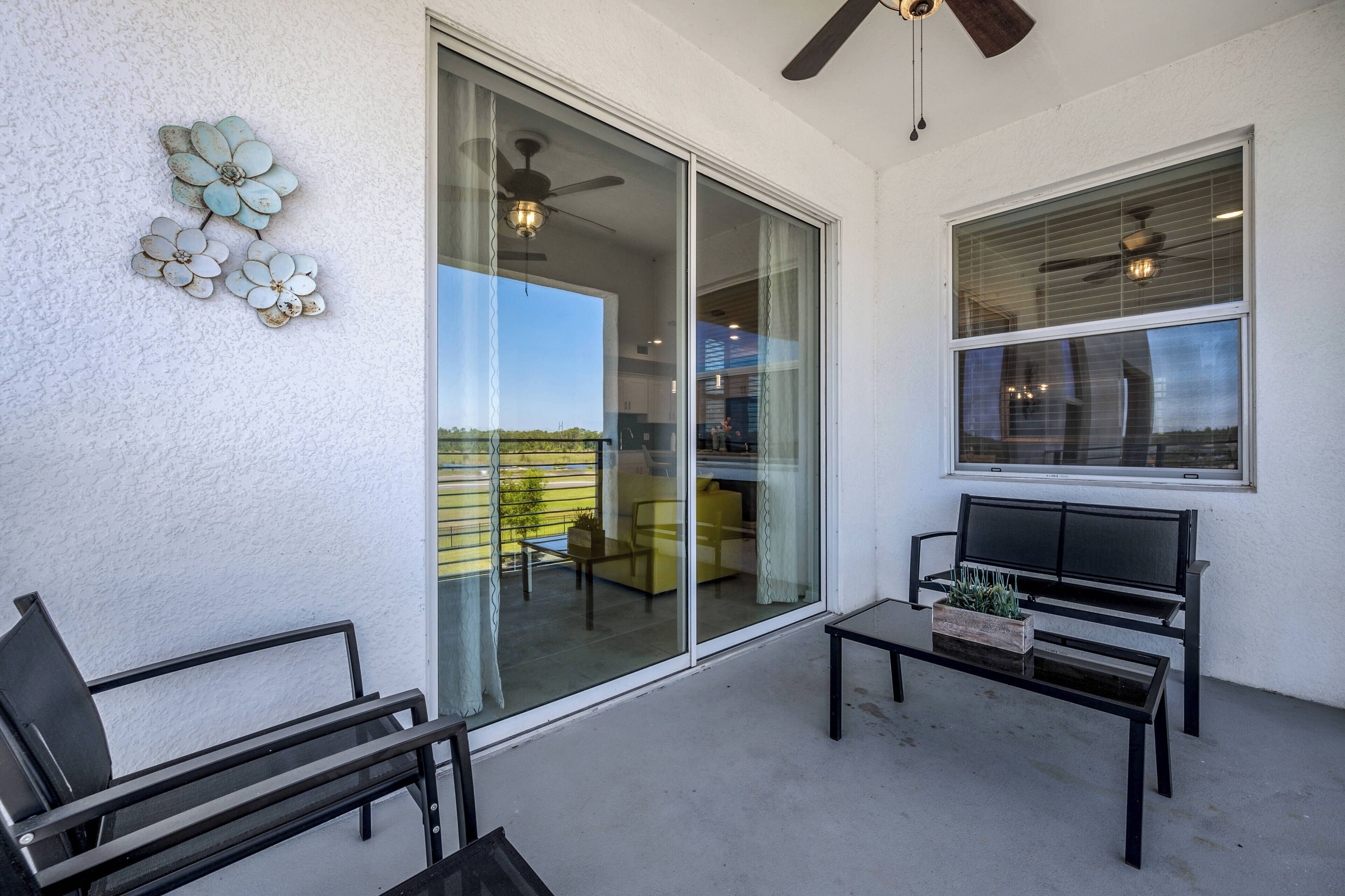 A balcony with a glass door, a ceiling fan, a bench, and a table with a plant.
