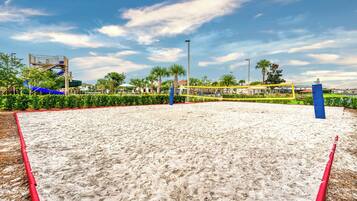 A sandy volleyball court with a net, surrounded by greenery and palm trees.