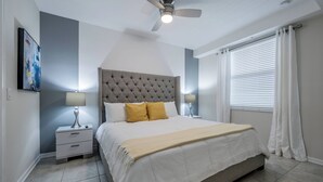 Un dormitorio con cabecera capitonada, cama con ropa de cama blanca y amarilla, dos mesitas de noche con lámparas y un ventilador de techo.