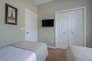 Un dormitorio con dos camas, un televisor montado en la pared y una puerta con un marco de fotos.