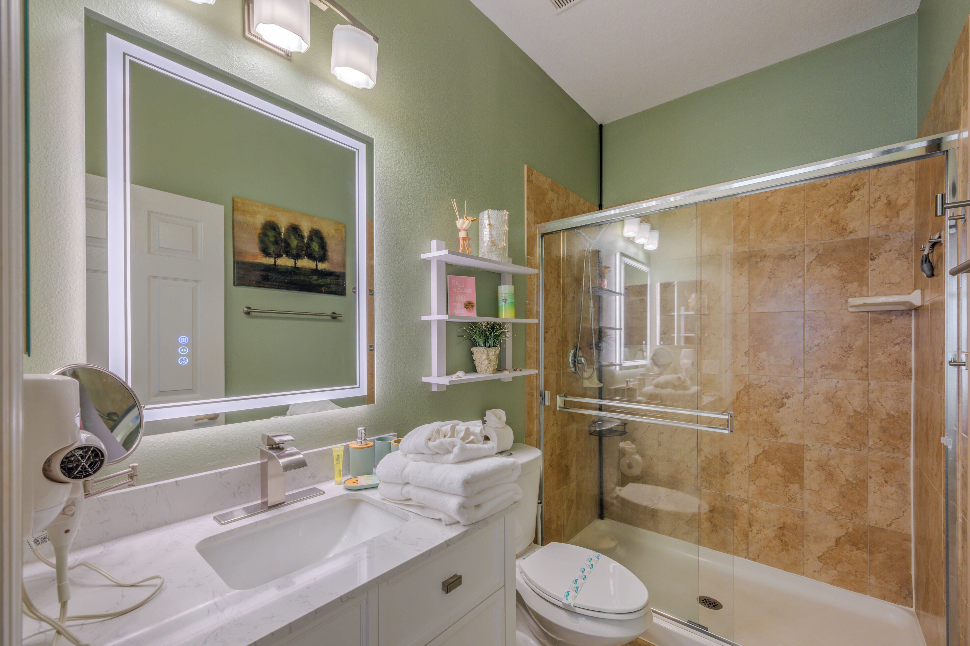 A bathroom with a large mirror, a sink, a toilet, and a shower area.