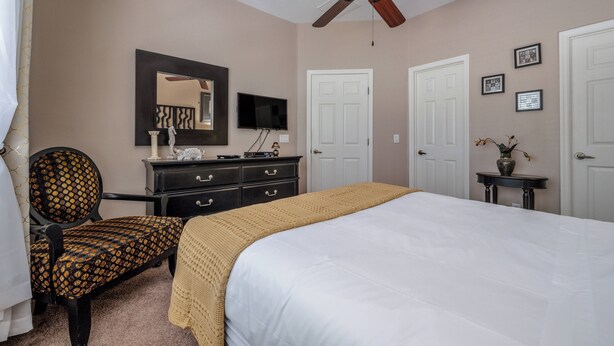 A bedroom with a bed, a chair, a dresser, a television, and a ceiling fan. - Ow2819 - 2BR Apartment With Balcony Near Disney (Kissimmee)