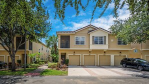 A two-story residential building with a beige facade, a red brick roof, and a garage with three doors. - Ow2819 - 2BR Apartment With Balcony Near Disney (Kissimmee)