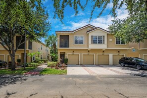 A two-story residential building with a beige facade, a red brick roof, and a garage with three doors. - Ow2819 - 2BR Apartment With Balcony Near Disney (Kissimmee)