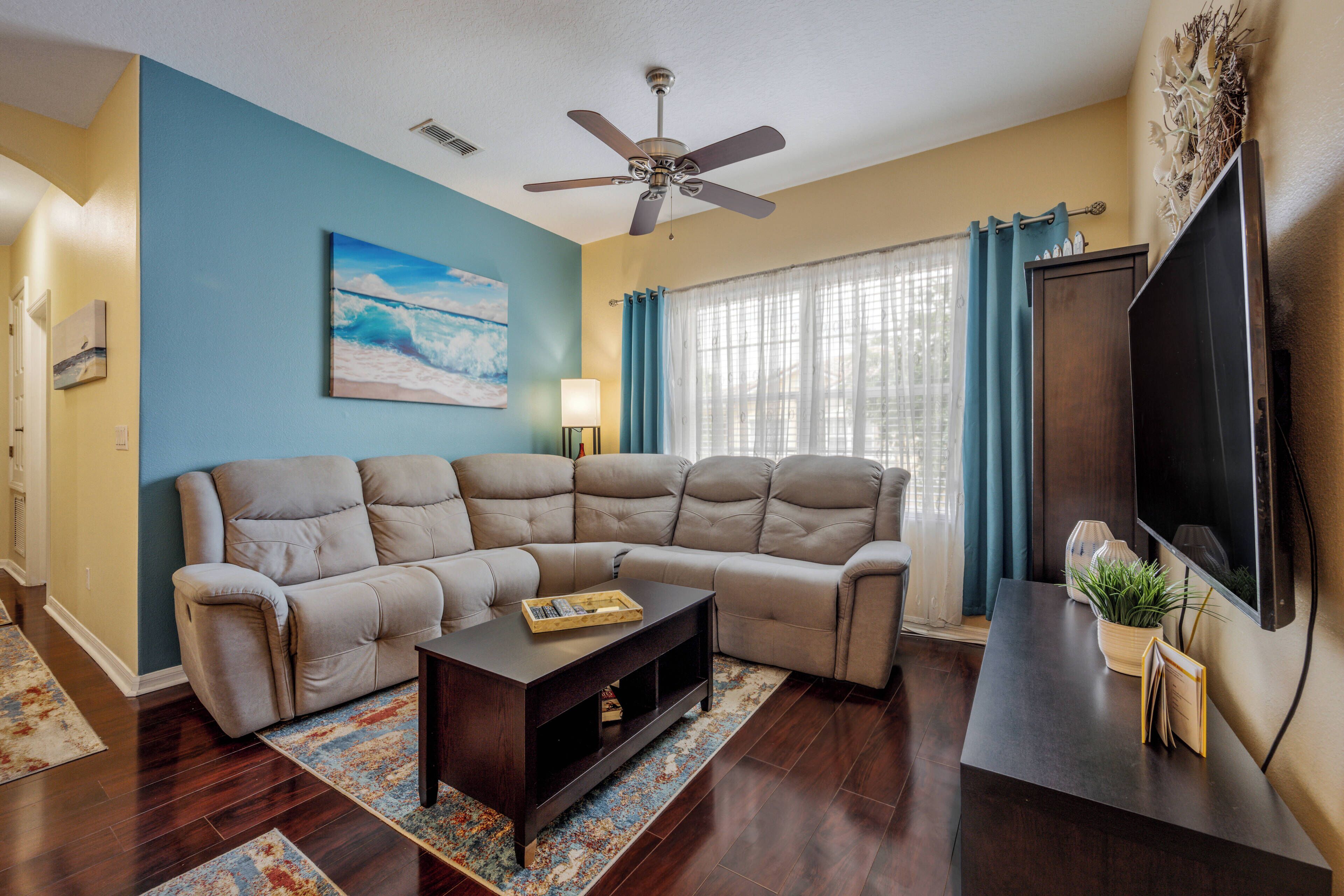 A living room with a sectional sofa, a coffee table, a flat-screen TV, and a ceiling fan.