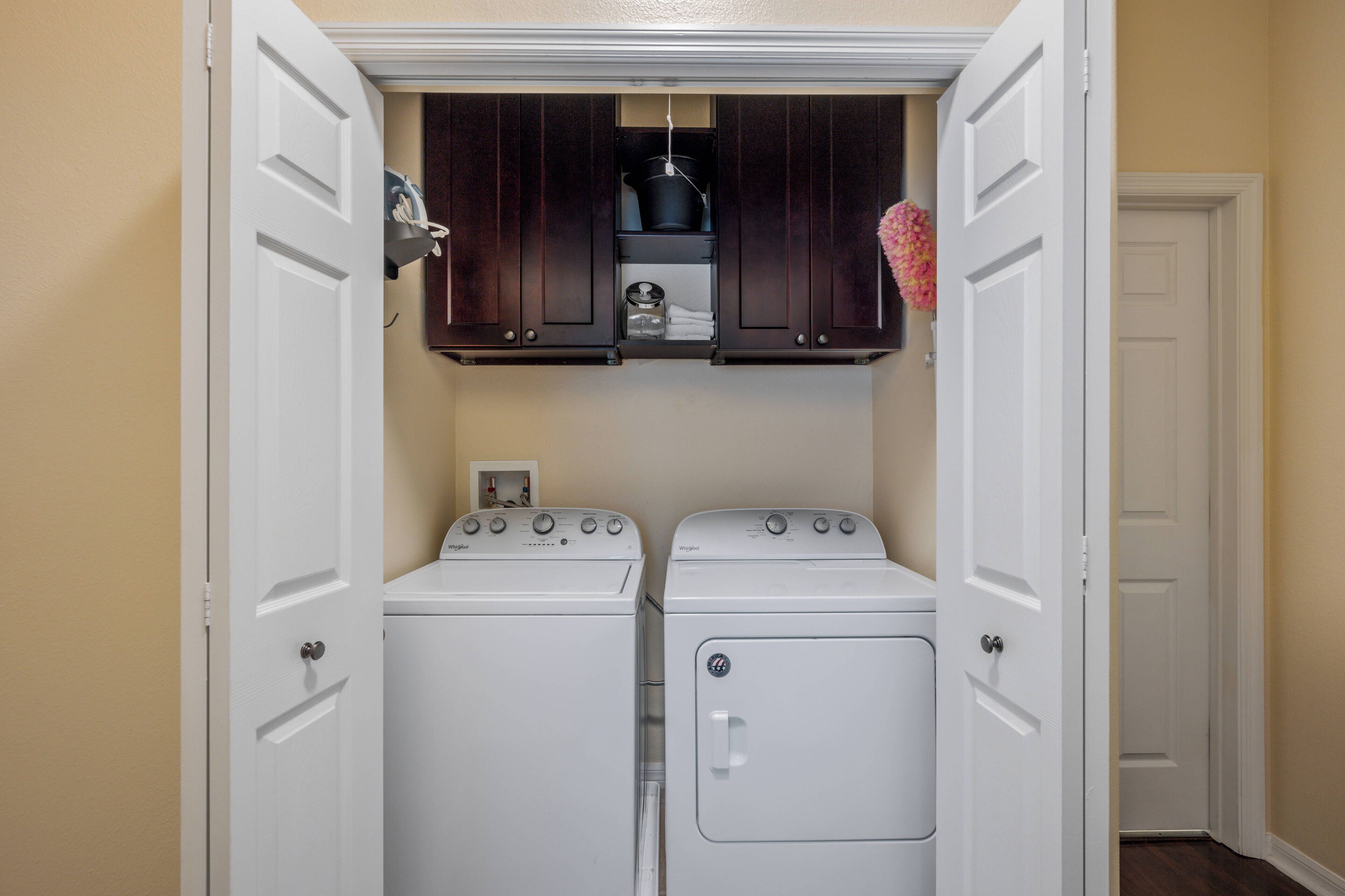 A laundry room with two white front-loading washers and a dark wooden cabinet above them.