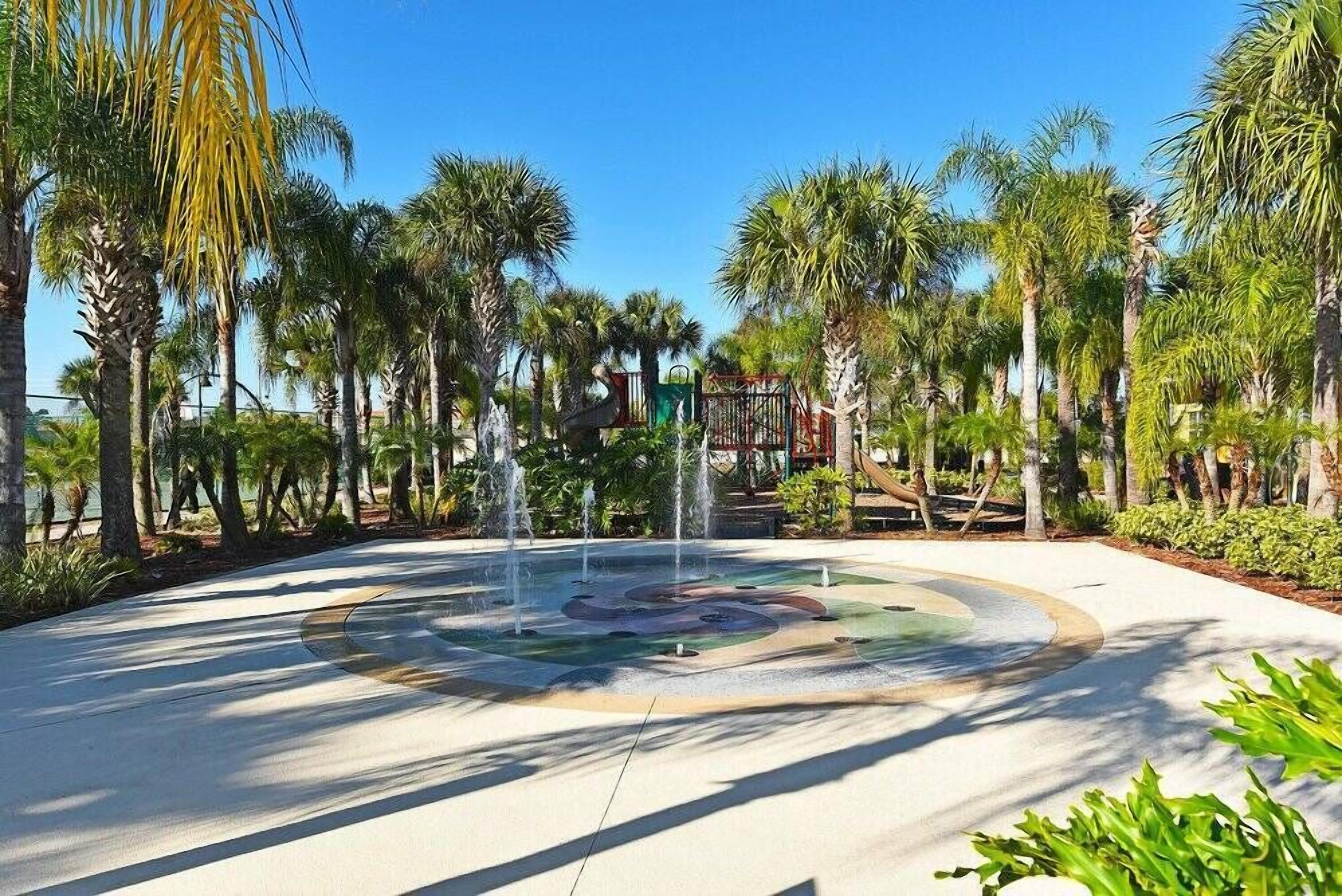 A circular water feature surrounded by palm trees and a playground in the background.