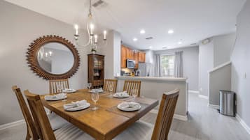 Un coin repas avec une table en bois dressée pour six personnes, entourée de chaises en bois. Un grand miroir avec un cadre décoratif est accroché au mur.