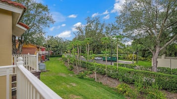 Un quartier résidentiel avec une pelouse bien entretenue, une rue bordée de voitures garées et une poubelle verte.
