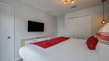 Une chambre à coucher avec un lit, un téléviseur fixé au mur, une armoire et une porte.