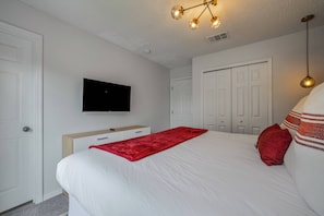 Een slaapkamer met een bed, een aan de muur bevestigde televisie, een kledingkast en een deur.