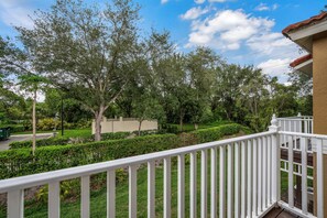A balcony with a white railing overlooking a well-maintained garden with various trees and shrubs. - Ei8555 - 3BR House Near Disney (Kissimmee)