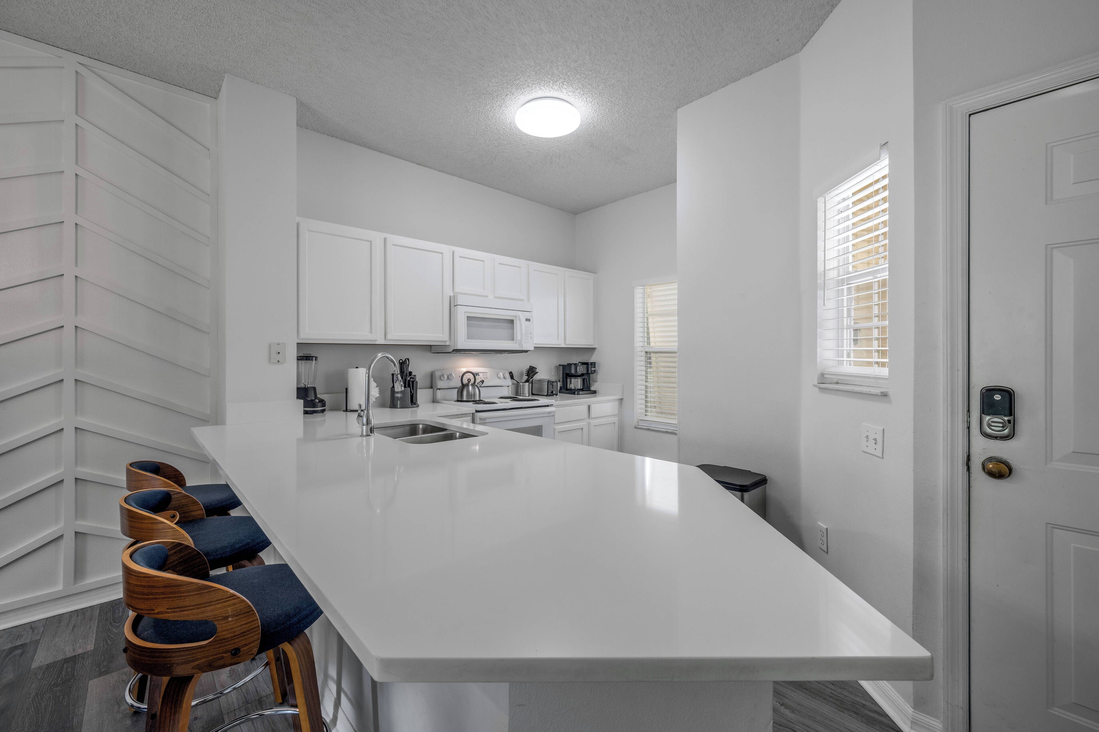 A modern kitchen with white cabinetry, a large island, and bar stools.