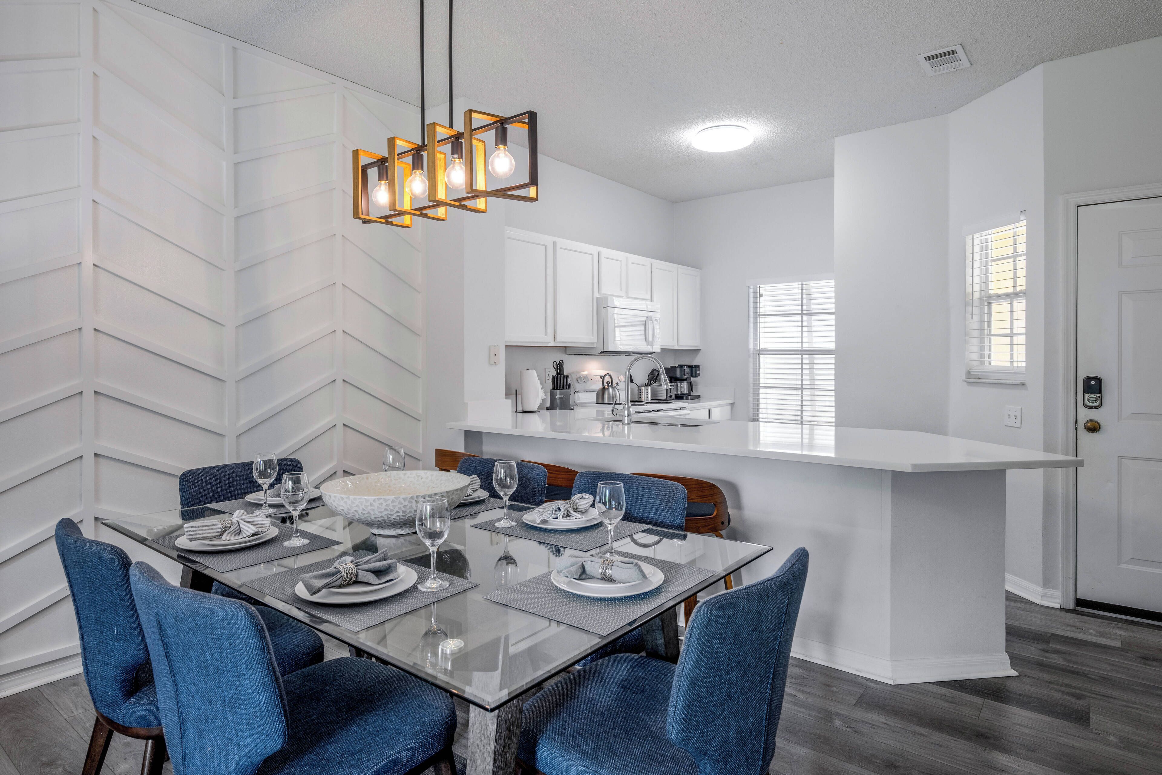 A modern kitchen with white cabinets, a central island, and a dining area with a glass table and blue chairs.