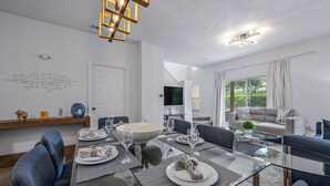 Et moderne spiseområde med et glasbord, blå stole og en hvid pendellampe.