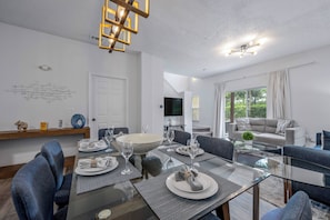Een moderne eetruimte met een glazen tafel, blauwe stoelen en een witte plafondlamp.